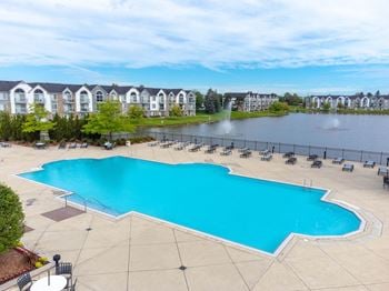 a large swimming pool with chaise lounge chairs next to a lake with apartment buildings in theat The Harbours Apartments, Clinton Twp, 48038
